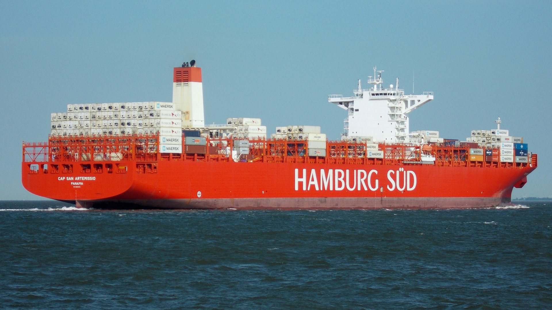 Real photograph of the container ship Cap San Artemissio at sea, carrying rows of white refrigerated containers with visible cooling units alongside other containers